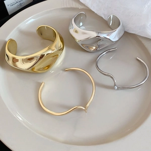 Detail view of wavy irregular open bangles in polished gold and silver finishes