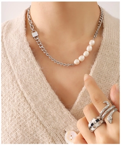 Detail of layered jewelry featuring a pearl link chain and bold textured statement rings