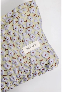 Detailaufnahme des floralen Jacquard-Stoffs mit lila Blumen auf gelber Kosmetiktasche