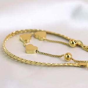 Detailed macro view of 18K gold heart charms and box chain on white silk fabric