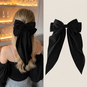 Detail of a large black satin bow hair clip with long ribbons in a half-up hairstyle