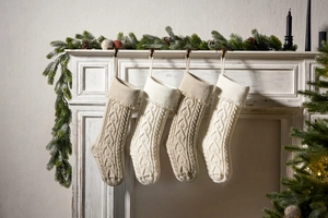 Close-up of four knitted Christmas stockings hanging on fireplace with pine needles