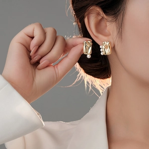 Detail showing gold-plated irregular earrings with elegant white pearls on a model