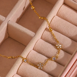 Detailed close-up of golden chain necklace with floral and round zircon charms in jewelry box