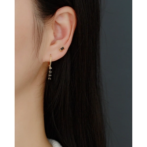 Macro view of gold hoop earrings with black rectangular zircon stones on ear