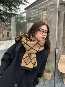 Close-up of a classic khaki and black checkered knit scarf on a model with wool coat