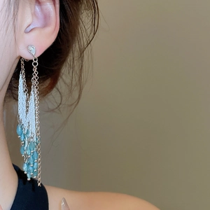 Détail de boucles d'oreilles longues dorées avec perles de cristal bleu clair en cascade