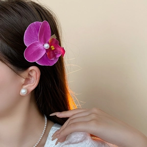Detail of orchid hair claw with purple petals and a central pearl decoration on a model