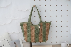 Detail of green striped straw tote bag featuring decorative tassels and wooden beads