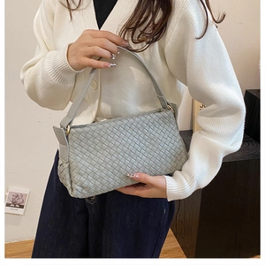 Dettaglio macro di una borsa a tracolla grigia intrecciata con texture artigianale di lusso