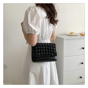 Detail of black pleated shoulder bag featuring elegant gold chain strap and quilted texture