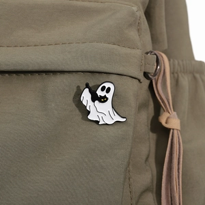 Close-up of a white ghost enamel pin with black cat on a green canvas background