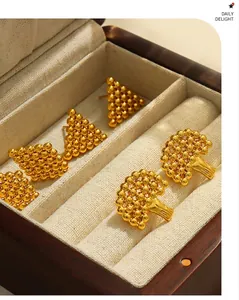 Macro detail of geometric gold-plated steel stud earrings in a wooden jewelry box