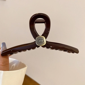Detail of dark brown acrylic hair claw clip with golden CD logo on a square metal plate