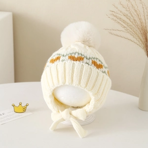 Detail of cream knit earflap hat with large faux fur pom-pom and geometric patterns