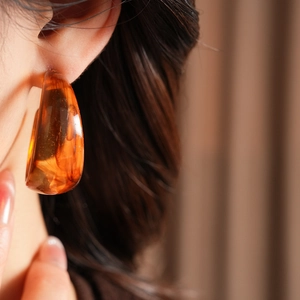 Side view of woman wearing chunky amber resin C-shape hoop earrings in retro style