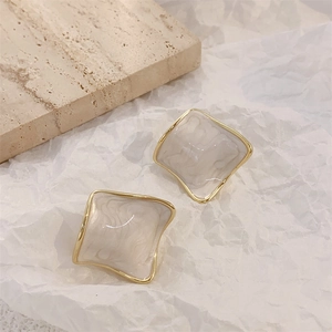 Detail of square gold-plated earrings with beige marble enamel on a stone texture