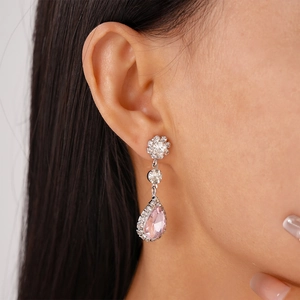 Close-up of dangling silver earrings featuring pink teardrop stones and flower accents