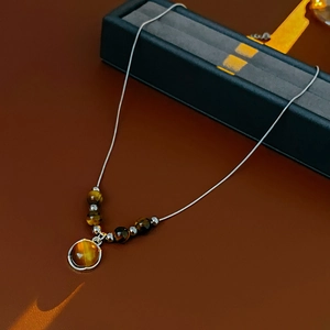 Macro detail of round brown tiger eye pendant with metallic beads on a silver chain