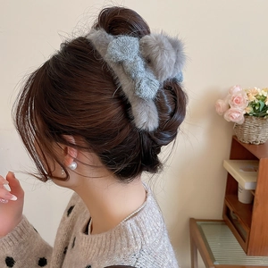Detail showing plush grey faux fur bow hair claw clip worn on a model in a cozy setting