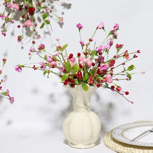 Dettaglio di fiori artificiali rosa e bacche rosse in un vaso di ceramica bianca