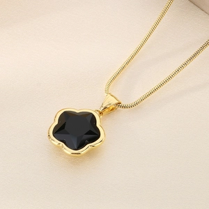 Detail shot of a golden snake chain necklace with a black clover leaf petal pendant