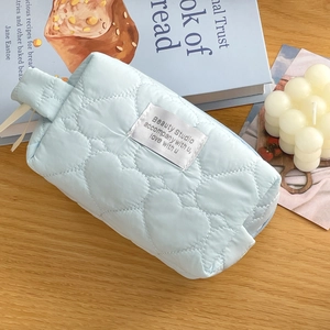 Detail view of light blue quilted cosmetic bag with heart embroidery and side handle