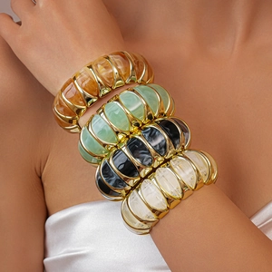 Close-up of stacked acrylic resin cuff bracelets with gold metal accents on model's arm