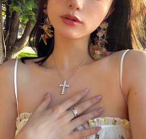 Detailed view of silver cross necklace with zircons and floral earrings on a model