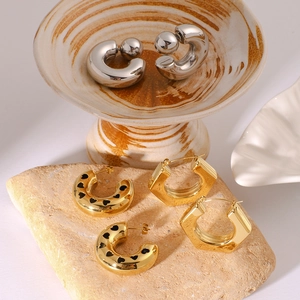 Three pairs of stylish C-shaped hollow earrings in gold and silver on a ceramic stand