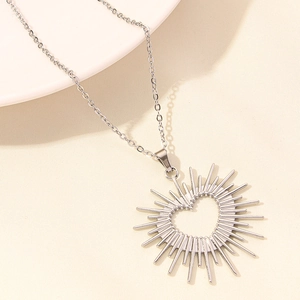 Macro detail of silver heart necklace with sunburst radial lines on a ceramic surface