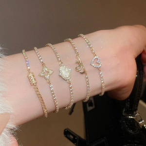 Close-up of five delicate gold bracelets with zircon heart, bow, and clover charms