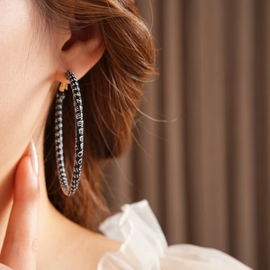 Close-up of model wearing black leather hoop earrings with white letter patterns