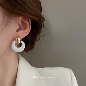 Detail of a minimalist white resin hoop earring with a sleek golden rectangular stud