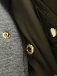 Makro-Detail aus grauem Strick, olivgrünem Nylon und goldenen Metalldruckknöpfen am Parka