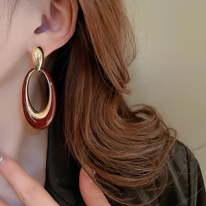 Detailed close-up of retro oval gold earrings with deep red enamel inlay on model