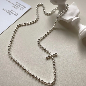 Minimalist silver beaded necklace with cross pendant on textured grey surface