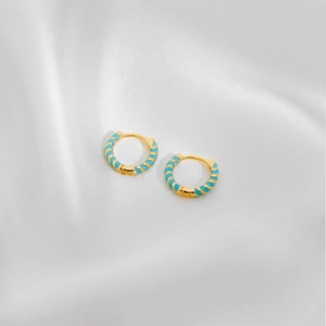 Detail of small gold hoop earrings with light blue enamel spiral texture on white silk