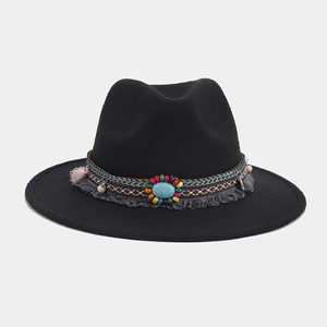 Detalle de sombrero fedora negro con banda étnica tejida, turquesa y borlas grises