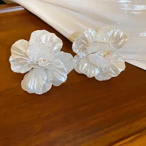 Elegant large shell flower earrings with center pearls on a luxury wooden pedestal