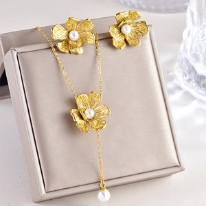 Vintage gold flower pendant necklace and pearl earrings set on a velvet jewelry box display