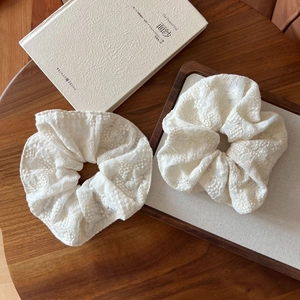 Close-up of two off-white lace scrunchies with intricate floral embroidery on a table
