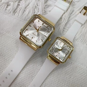 Dettaglio di due orologi quadrati dorati con cinturini in silicone bianco su tessuto