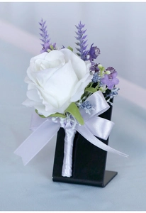 Close-up of white artificial rose boutonniere with lavender accents and silk bow detail