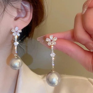 Détail de boucles d'oreilles argentées avec clou en fleur scintillante et grosse perle blanche