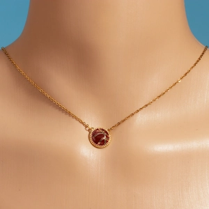 Detail of gold necklace with red gemstone and leaf pattern on a beige mannequin