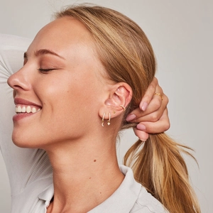 Close-up of a model wearing a set of gold earrings with moon and heart charms and a ring