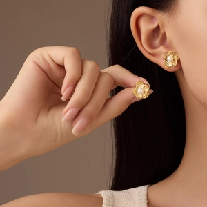 Elegant gold flower earrings with central white pearl shown on a model's ear