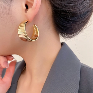 Detailed view of large gold-toned ribbed C-shape hoop earrings worn by a model