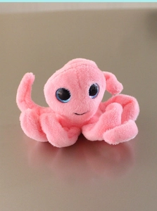 Close-up of a soft pink plush octopus fridge magnet with big eyes on metal surface